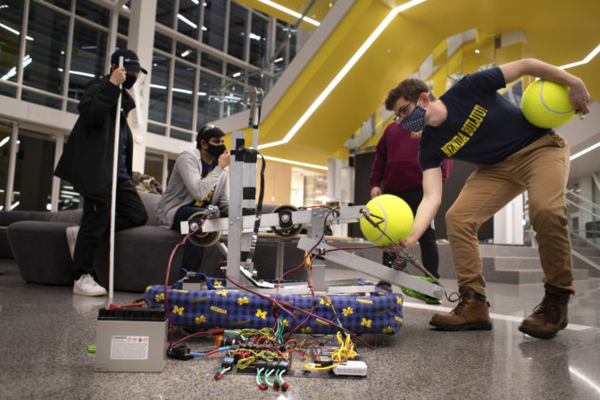 Taubitz of the FAMN team feeds a ball to their robot. In competition, the spinning green wheels visible near Taubitz’s foot will move balls from the floor over the maize-and-blue bumper and into the robot. At the controller’s command, the orange doors in the middle of the robot will open, releasing the ball into the shooting chamber. There, the fast-spinning wheels at the top of the robot will shoot the ball toward the target.